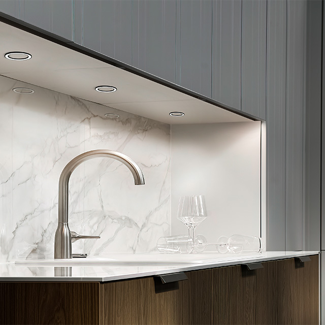 A modern kitchen featuring an elegant sink, a marble worktop and tasteful lighting beneath the wall units