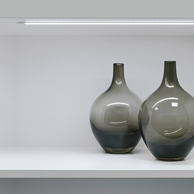 Das beleuchtete Vario D10 Regal präsentiert stilvolle Vasen in eleganten Grautönen, die den Raum harmonisch akzentuieren.