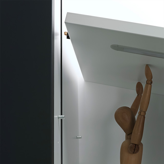 Eine Gliederpuppe greift nach einem oberen Regal im Vario-D10-Regal, das in einem modernen Raum installiert ist.